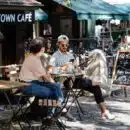 man and woman sitting in front of folding table in front of cafe with green awnings