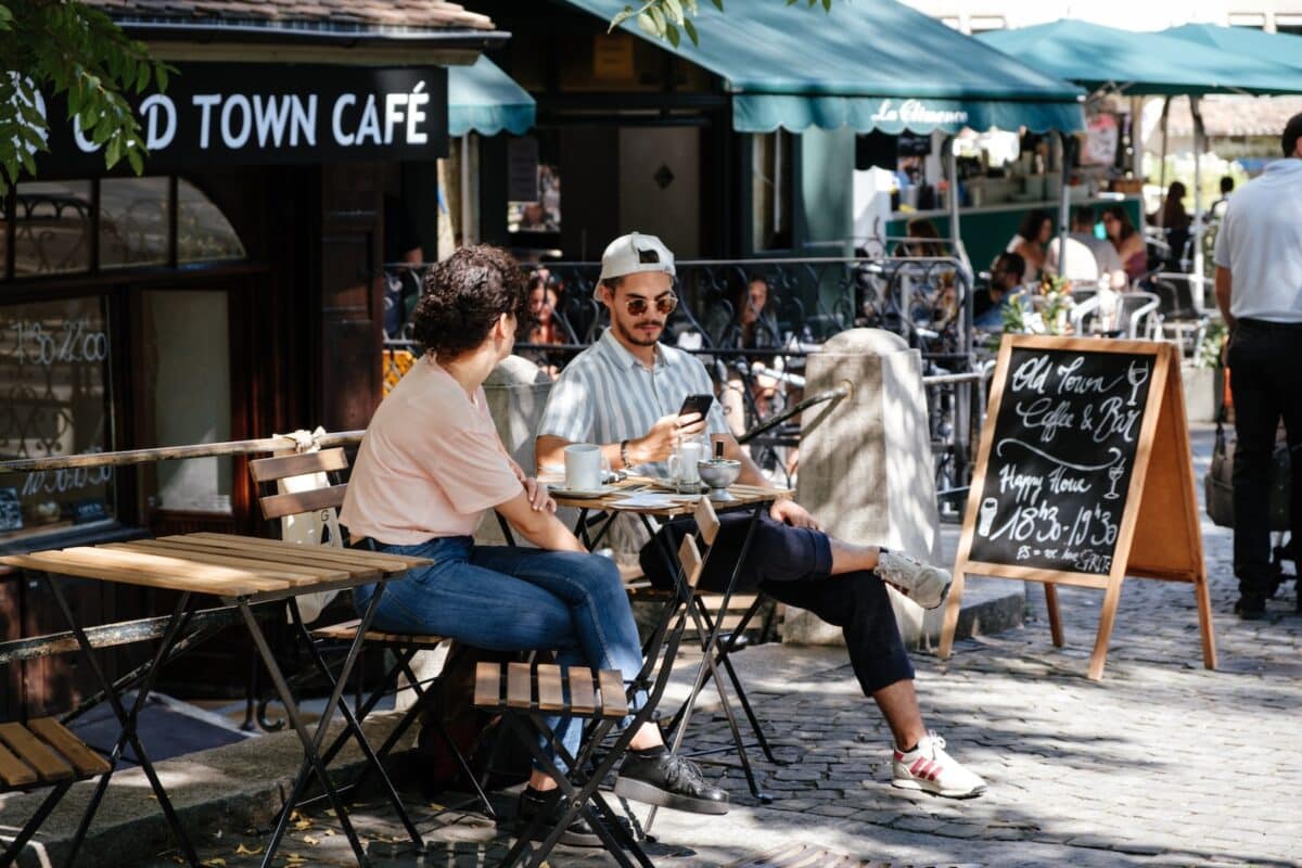 man and woman sitting in front of folding table in front of cafe with green awnings